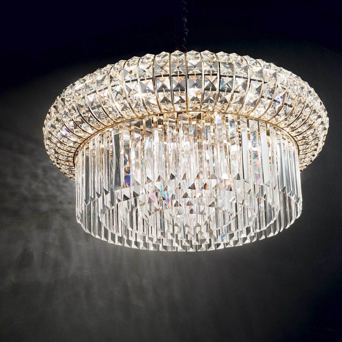 Close up of drum shaped golden chandelier with square and round crystals on black background