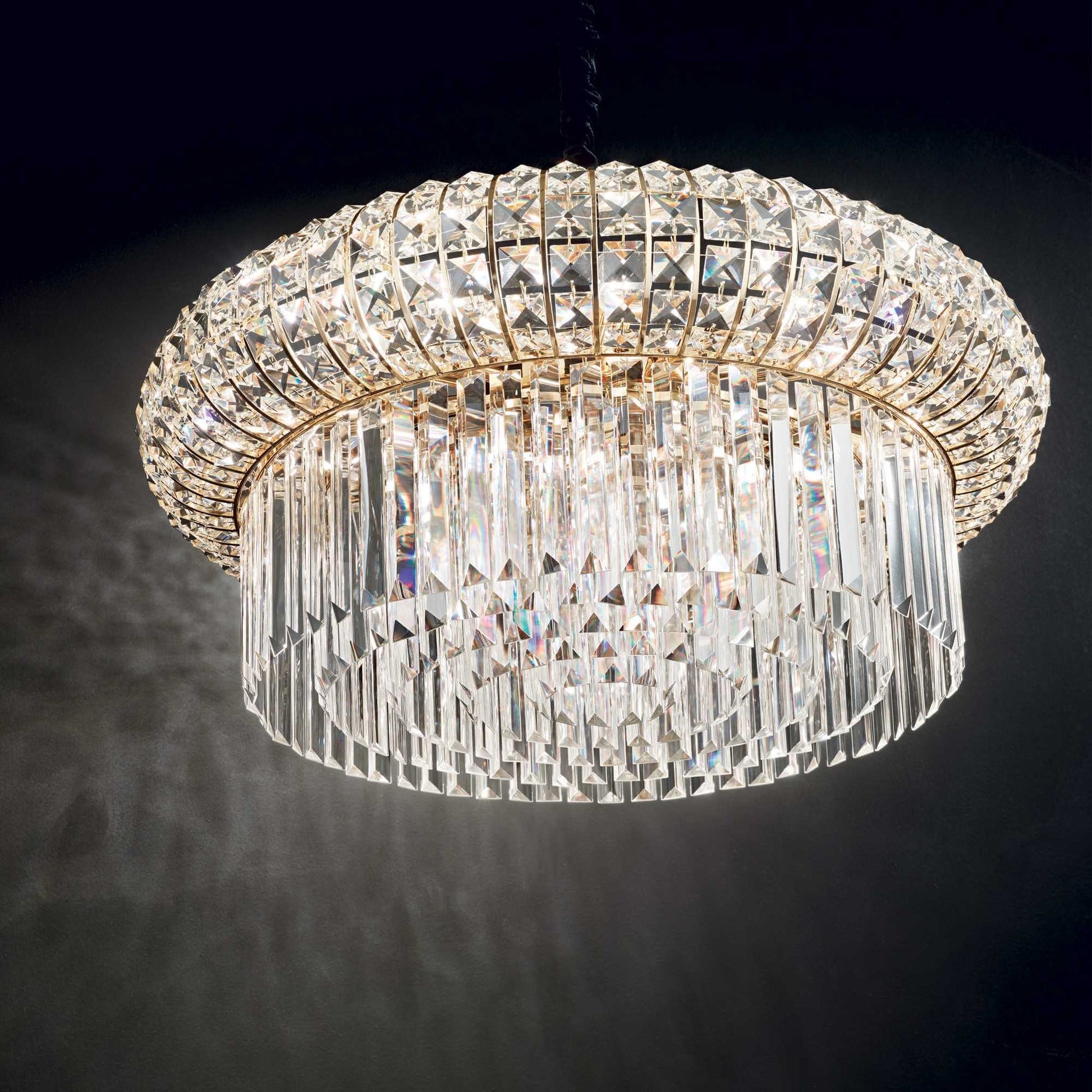 Close up of drum shaped golden chandelier with square and round crystals on black background
