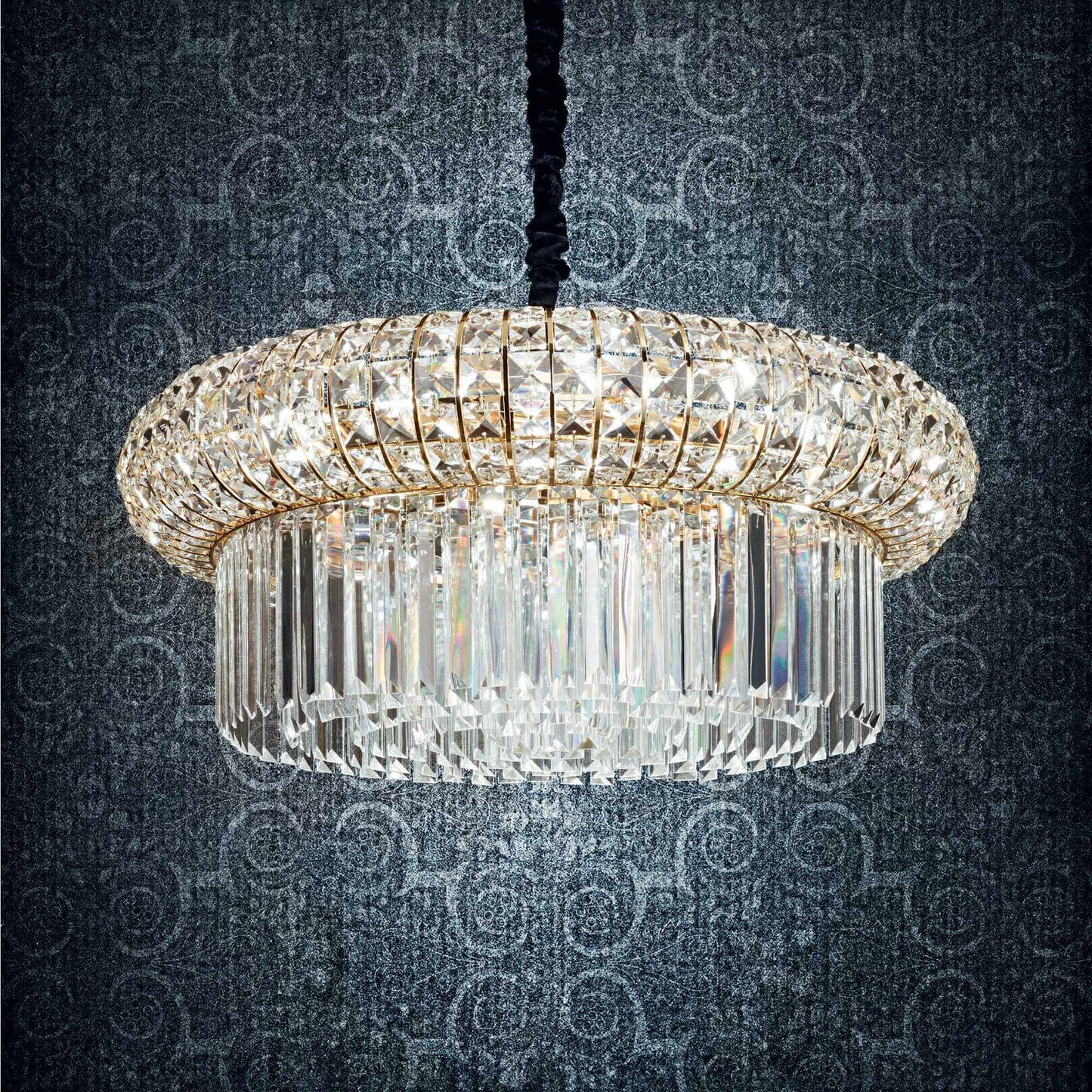 Drum shaped golden chandelier with square and round crystals on a dark blue patterned background