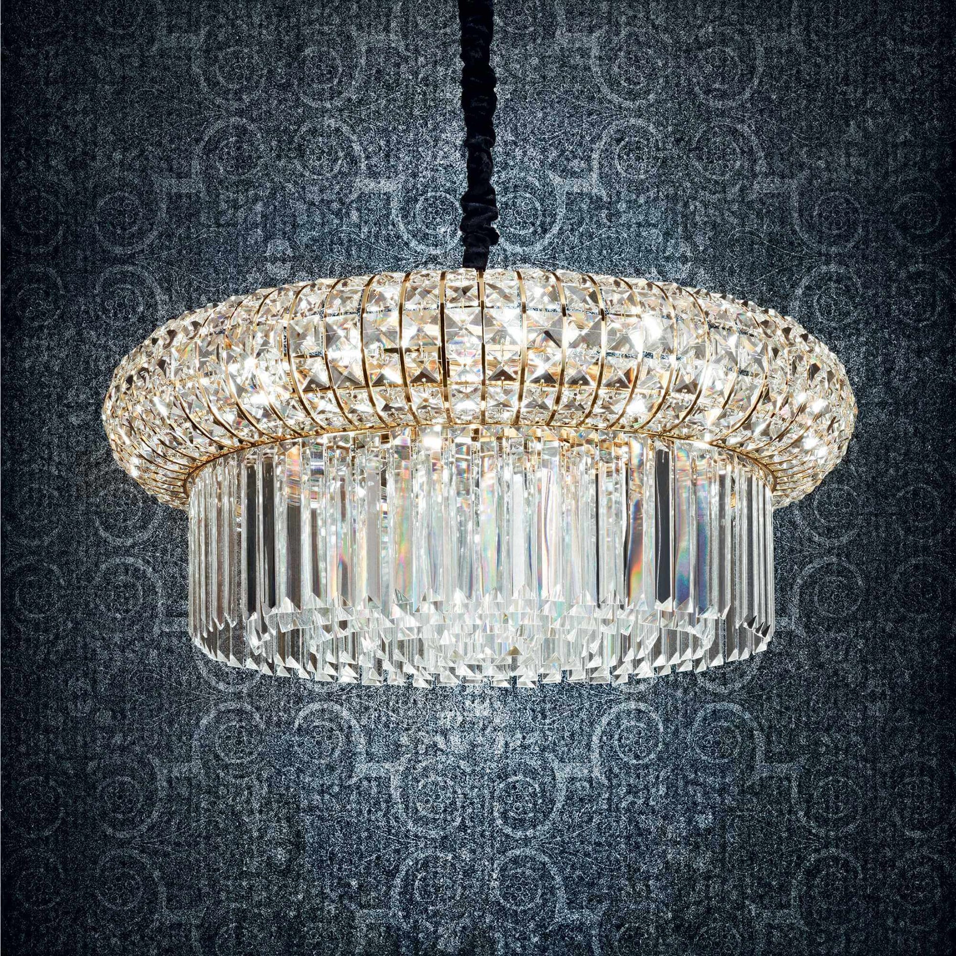 Drum shaped golden chandelier with square and round crystals on a dark blue patterned background